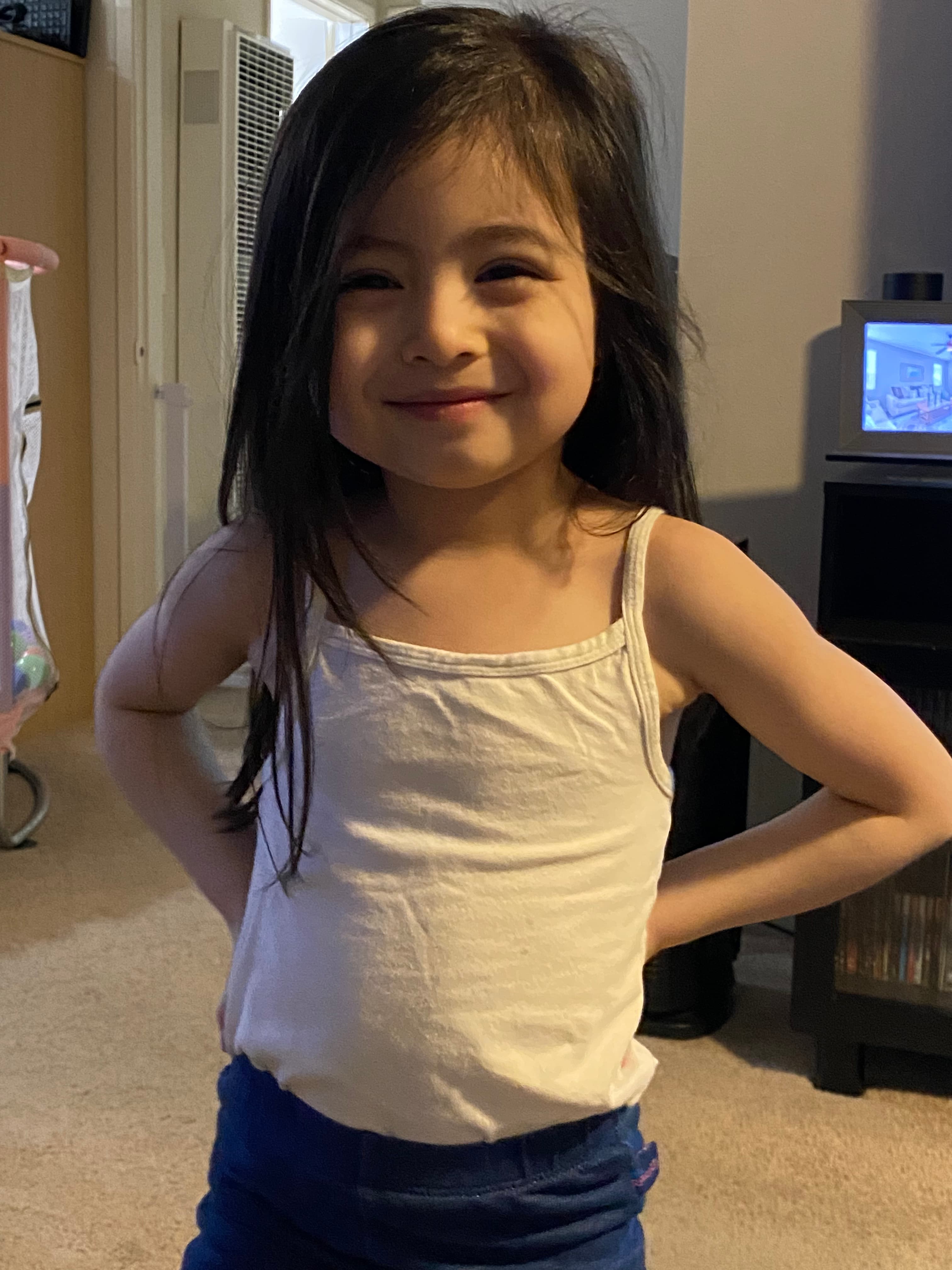 Smiling young girl in a white tank top posing with hands on her hips.
